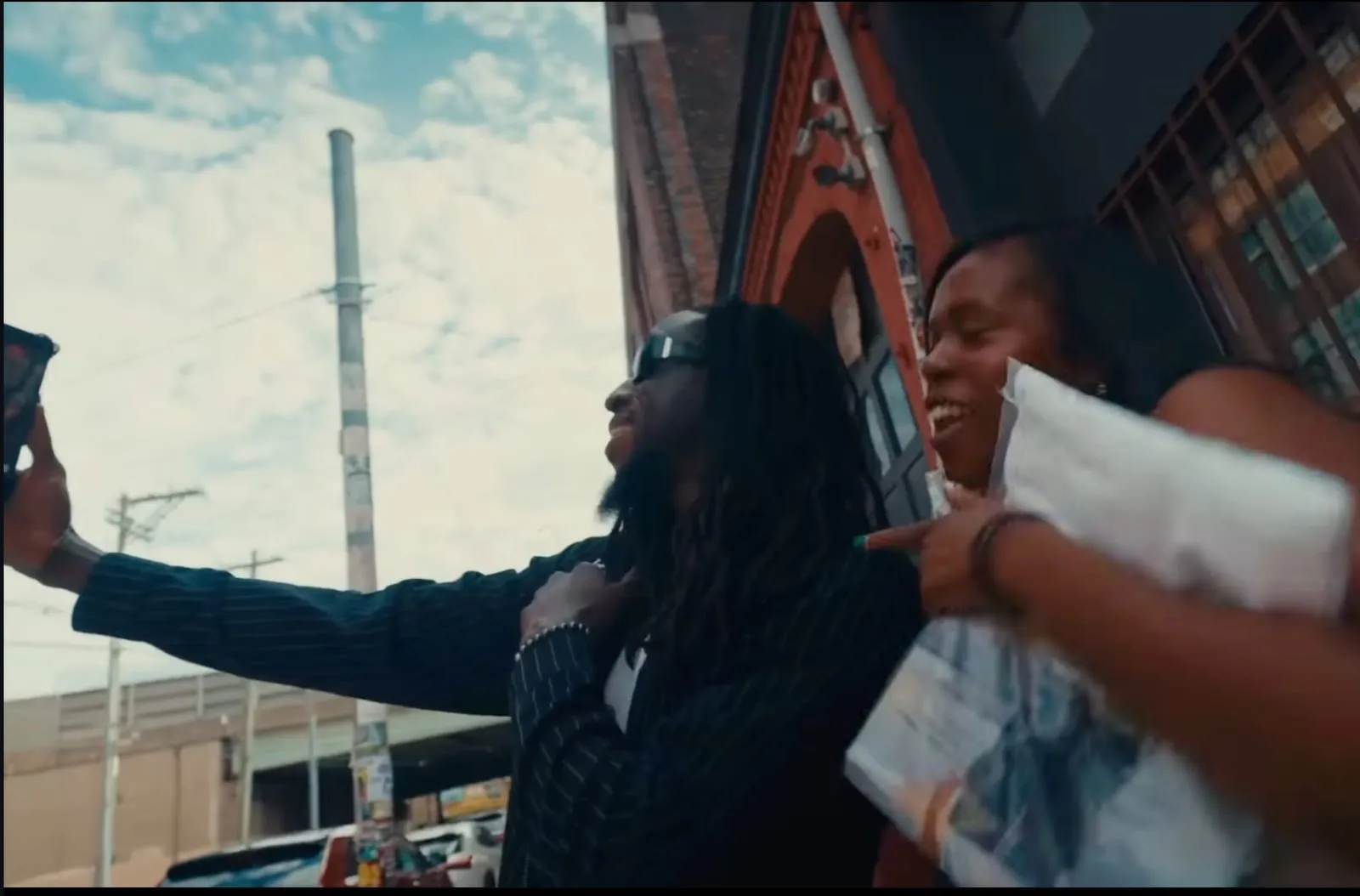 Kofi Bonsu taking a selfie with a fan on the street, from the “Perfect World” visualizer